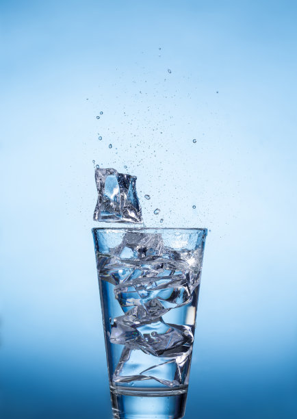 将装有冰块的水杯溅到蓝色背景上图片下载