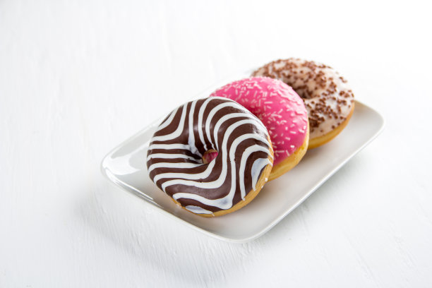 白色桌子上的盘子里放着三个彩色的甜甜圈图片下载