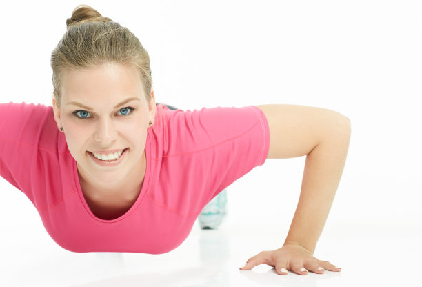 一个年轻的微笑运动女孩的肖像做俯卧撑孤立在一个白色的背景。健康的生活方式的概念。图片下载