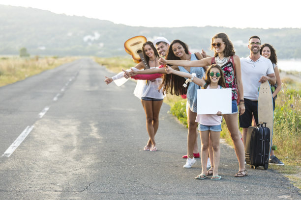 朋友们举着牌子，在乡村路上搭便车图片下载