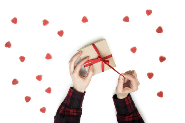 男人的手打开了红丝带的礼物。情人节背景与甜蜜的心模式孤立在白色顶视图。爱情主题平铺图片下载