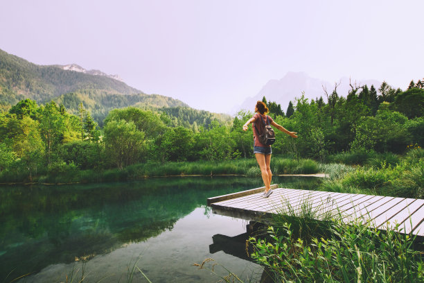 一名年轻女子站在木桥上，双手高举，背景是大自然。图片下载