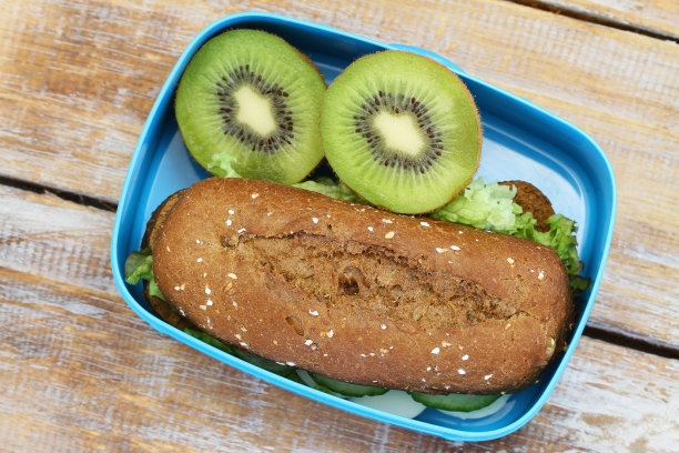 健康午餐盒，包括棕色芝士卷和两半猕猴桃图片下载