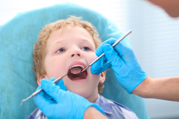 儿科牙医在牙科诊所的椅子上检查一个小男孩的牙齿。图片下载