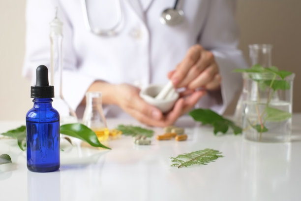 科学家或医生在实验室用草药制作草药。替代疗法。展示手和听诊器。带瓶子容器。素材图片