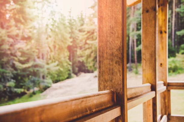 一个木制阳台护墙的特写。松树林在阳光下的背景。图片下载