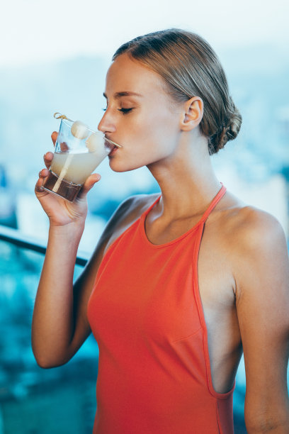 穿着礼服的年轻女子在阳台上喝鸡尾酒图片下载