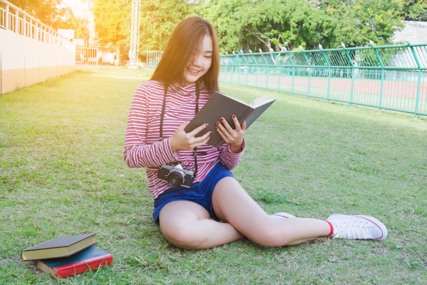 十几岁的女孩在草坪上读课本图片下载