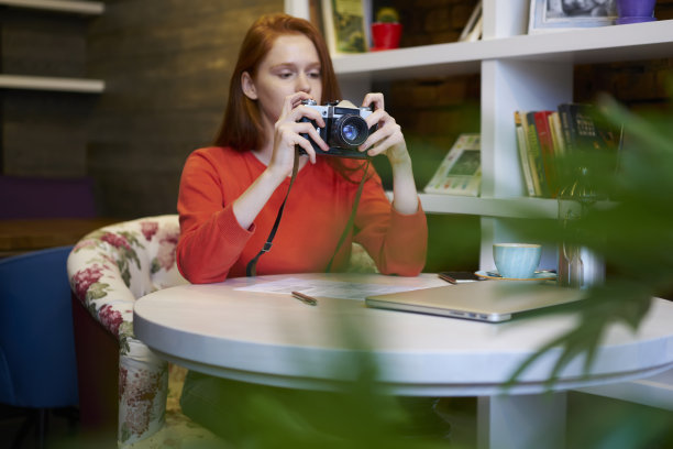 红发迷人的时髦女孩设置复古相机，让好照片坐在舒适的地方，年轻迷人的女人享受闲暇时间和最喜欢的爱好在舒适的图书馆图片下载