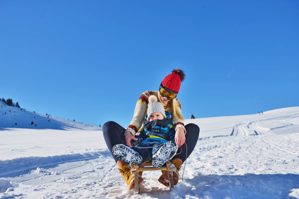 阳光明媚的冬日里，快乐的母子在雪地里玩雪橇的照片图片下载