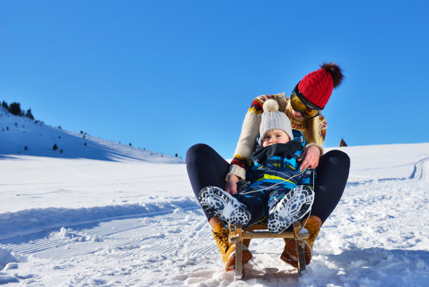 阳光明媚的冬日里，快乐的母子在雪地里玩雪橇的照片图片下载