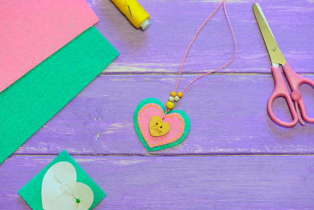 可爱的心形吊坠项链。情人节吊坠项链，由毛毡，珠子和木制按钮与铭文的爱。孩子工作。礼物送给母亲。快速和简单的手工艺的孩子图片下载