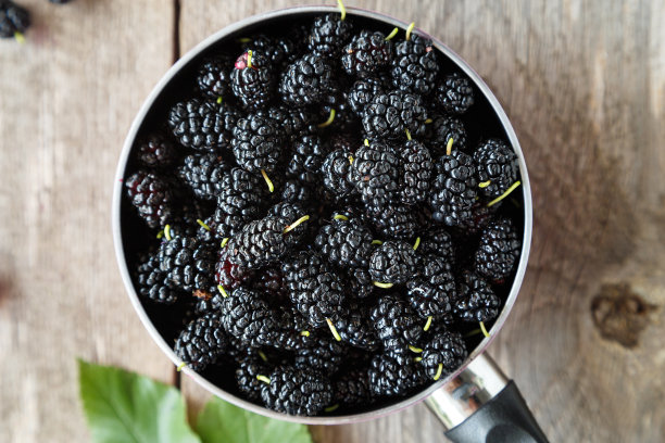 木桌上的粉红花盆里装着黑桑葚。图片下载