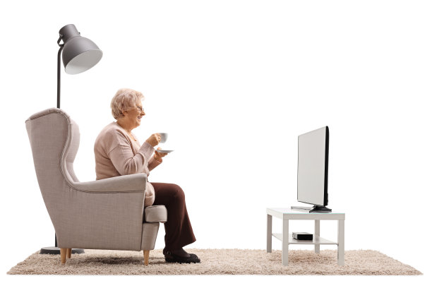 老妇人坐在扶手椅上，手里拿着一个杯子看电视图片下载