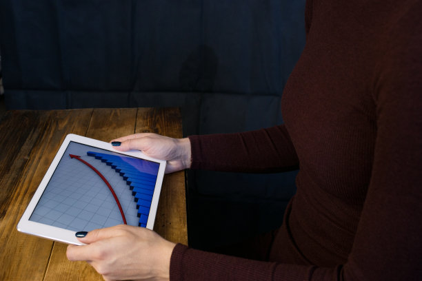 用平板电脑工作的女孩。曲线上升。桌子，木制，背景黑色。图片下载