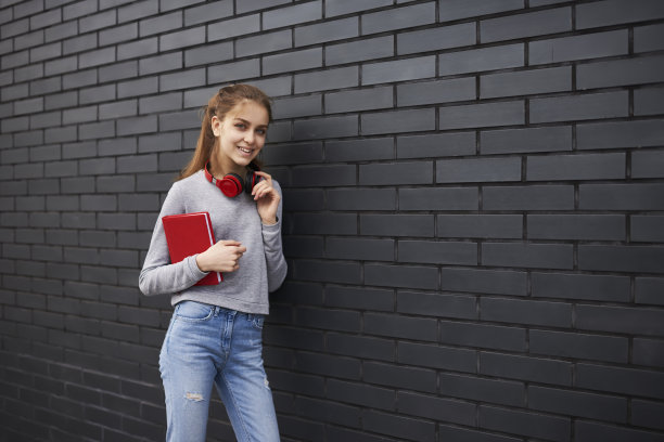 微笑迷人的女学生漫步在户外的城市设置促销背景，抱着书，穿着时髦的时髦女孩享受好天气散步在复印空间附近的广告图片下载