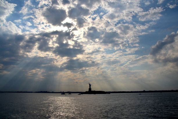 这是自由女神像的剪影，阳光照射在周围的水面上图片下载