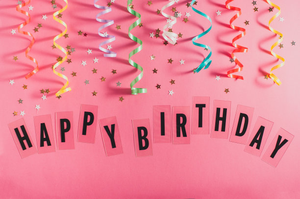 五颜六色的派对彩带，金色的小星星，粉红色背景上写着生日快乐。女孩生日的概念。平的。素材图片