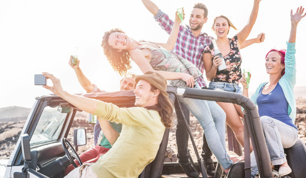 一群快乐的朋友在沙漠上敞篷吉普车聚会-旅行的人有乐趣喝香槟和自拍-友谊和度假概念-关注男人的脸与手机图片下载