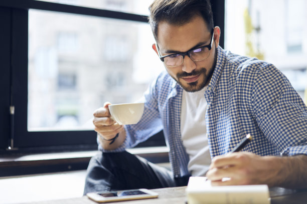 有才华有创意的男性市场营销专家，为活动公司的广告活动绘制插画，在笔记本上画素描，让人在阳光明媚的天气里坐在现代办公空间的桌子旁图片下载