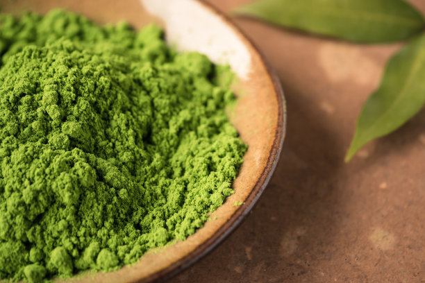 近距离观察瓷盘里的绿茶粉和桌上的叶子。素材图片
