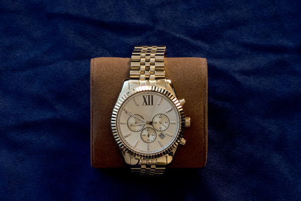 黄金腕表与一个黄色的金属手镯在一个深蓝色的背景素材图片