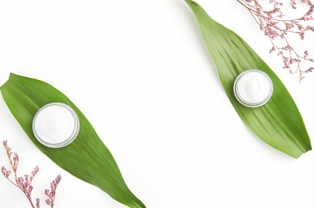 白色奶油瓶放置，空白标签包装，以绿叶和花朵为背景。天然美容产品的概念。图片下载