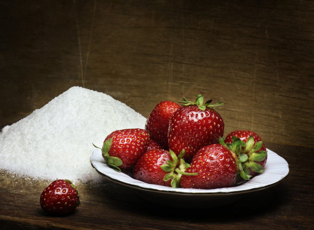 木桌上放着草莓和糖的盘子。图片下载