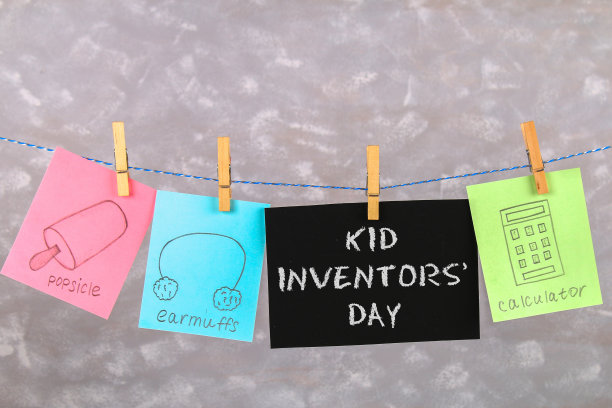 衣服钉上挂着笔记，上面画着孩子们的发明——popsikl, Earmuffs，计算器，灰色背景。短信-孩子发明家日。图片下载