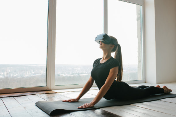 一个年轻美丽的女孩戴着虚拟现实眼镜远程做瑜伽和有氧运动。未来科技的概念。现代的成像技术。在单一运动类远程。图片下载