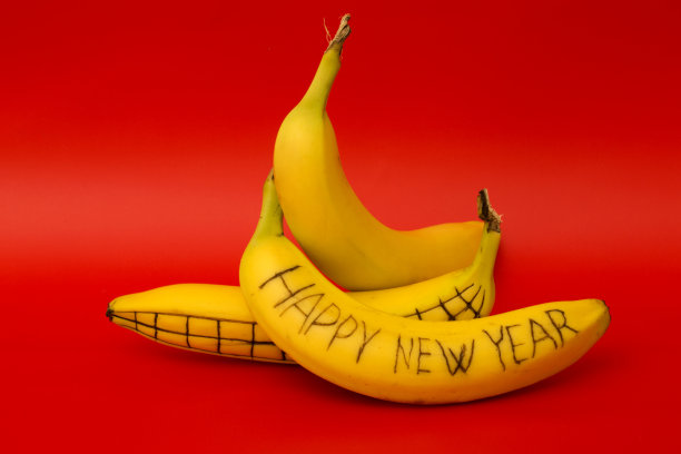 红色背景上画着“新年快乐”字样的三根成熟香蕉图片下载