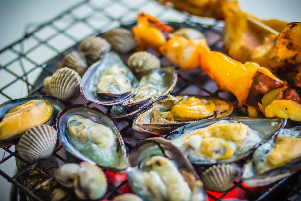 烧烤鱿鱼，贻贝和蛤蜊在木炭炉晚上聚会。海鲜烧烤派对，鱿鱼，鱿鱼，贻贝和蛤在火上烤。BBQ概念，选择性聚焦。图片下载