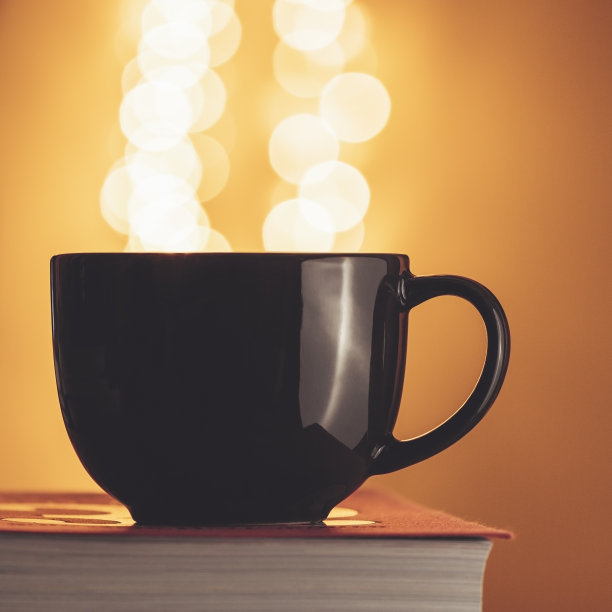 在模糊的灯光下，那杯黑茶映在一本书上。图片下载