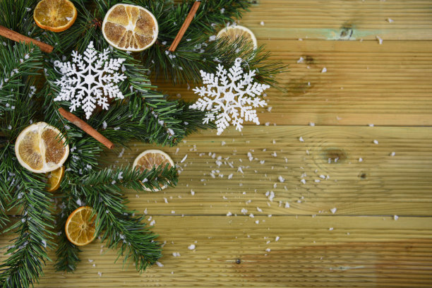 这张圣诞美食照片的背景是绿色的树枝和肉桂枝、橙色的切片和白色的雪花装饰图片下载