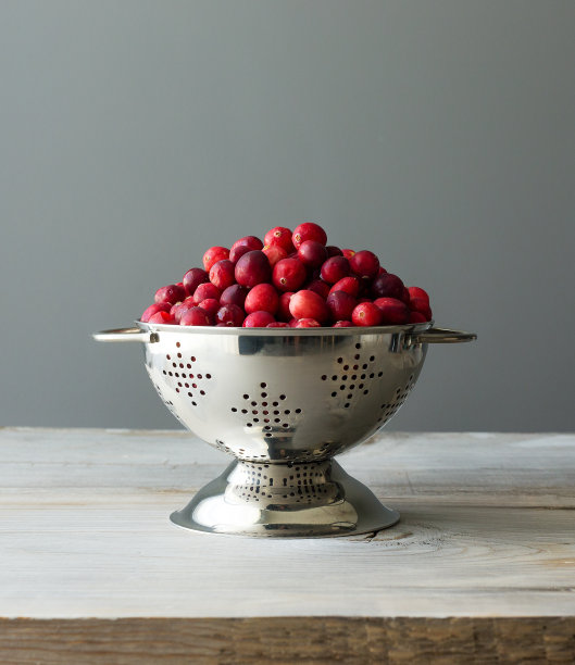 新鲜的生蔓越莓放在一个小不锈钢滤锅里，背景是灰色。素材图片