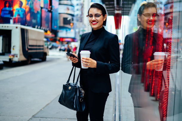 这是一幅半长肖像，照片上的女性经理身着优雅的套装，站在街上使用网上银行应用程序，微笑着看着摄像头，在大城市里用智能手机导航图片下载
