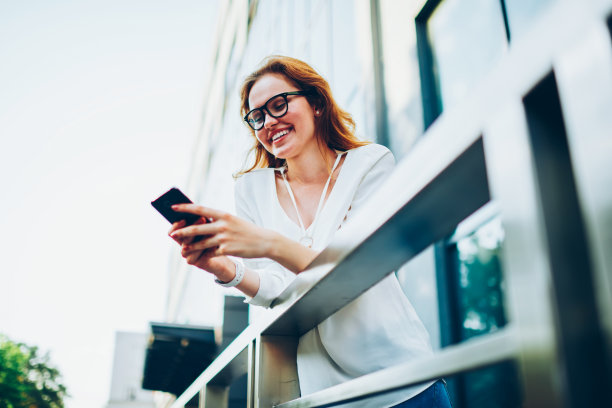 快乐的时髦女孩通过智能手机在社交网络上阅读新闻站在户外，微笑的女人与朋友聊天发送信息和照片享受互联网和休闲在城市街道上图片下载