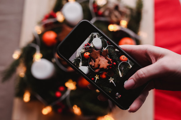 女人的手拿着圣诞晚会用姜饼饼干制作的新年花环的手机照片。蛋糕在一堆上面。圣诞夜的设计图片下载