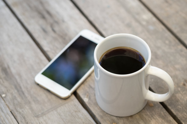 一杯热黑咖啡和智能手机放在木桌上。图片下载
