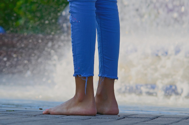 靠近腿和脚的年轻女子在蓝色牛仔裤站与溅水的背景。图片下载