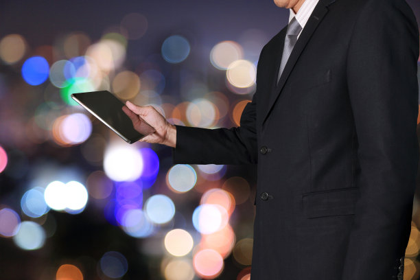 在模糊抽象的夜景背景下，商人将平板设备视为技术理念。图片下载