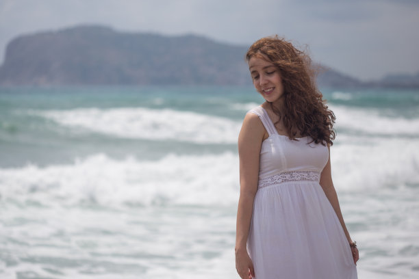 年轻的黑发女子与波浪形的头发穿着白色的连衣裙图片下载