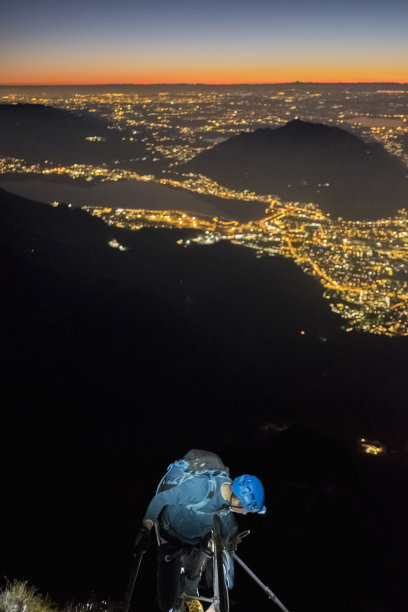 黄昏时分，登山者登上山顶，俯瞰被照亮的城市图片下载