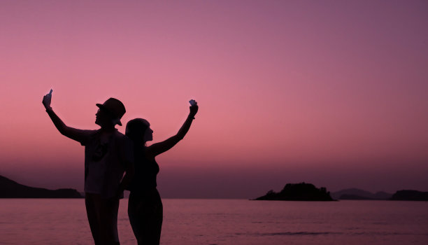 爱情概念，剪影的夫妇有浪漫的时刻和使用智能手机在黄昏海，情人节背景图片下载