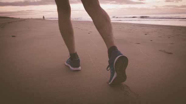 日出时在海滩上跑步的那个男人的腿。图片下载