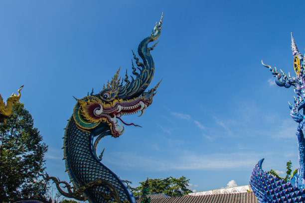 在阳光明媚的日子里，美丽的蓝色那迦雕塑，蓝天白云，在泰国清莱的公共寺庙，Wat Rong Sua Ten。那伽是一种非常大的蛇，在佛教寺庙中可以找到。图片下载