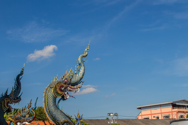 在阳光明媚的日子里，美丽的蓝色那迦雕塑，蓝天白云，在泰国清莱的公共寺庙，Wat Rong Sua Ten。那伽是一种非常大的蛇，在佛教寺庙中可以找到。图片下载