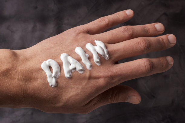 痛苦这个词是用奶油写的。涂了乳霜或药膏的男人干燥的手会感到疼痛。灰色背景图片下载