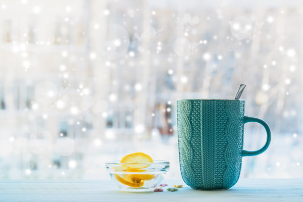 一杯热腾腾的茶放在木桌上，映衬着模糊的窗户背景，是冬日里圣诞节的背景图片下载