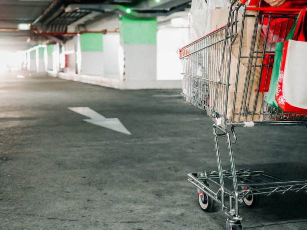在商场停车场，用柔和的对焦车行道和灯光背景将购物车里的全部物品拉近图片下载